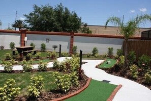 A backyard with a putting green, a small pond, and a patio area.