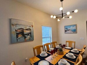 A dining room with a table set for six, wooden chairs, a chandelier, and two paintings on the walls.
