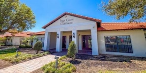A building with a sign reading 'Ditch Grove Clubhouse,' featuring a red-tiled roof, white walls, and a paved entrance area with a pathway. - Executive Home in Gated Community w pool spa, games room, close to shops (Clermont)