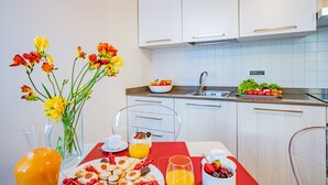 A modern kitchen with white cabinets, a sink, and a breakfast setup including a fruit bowl, a plate of cookies, and a glass of orange juice. - Ca' Del Monastero 8 Collection (Venice)