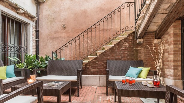 A patio area with wicker furniture, a brick wall, and a spiral staircase. - Ca' Del Monastero 8 Collection (Venice)