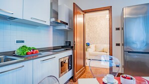 A modern kitchen with a built-in oven, a refrigerator, and a dining area with a table and chairs. - Ca' Del Monastero 8 Collection (Venice)