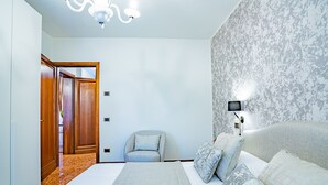 A bedroom with a bed, a chair, a nightstand, a lamp, and a door. - Ca' Del Monastero 8 Collection (Venice)