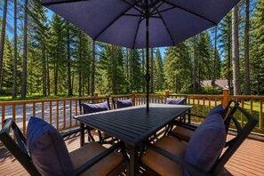 An outdoor deck with a table and chairs, surrounded by a wooden railing and a view of a forest. - Sauna | Deck | Firepit | Near Lakes | WIFI | BBQ (Leavenworth)