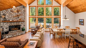 A spacious interior with a stone fireplace, wooden ceiling, large windows, and a dining area. - Sauna | Deck | Firepit | Near Lakes | WIFI | BBQ (Leavenworth)