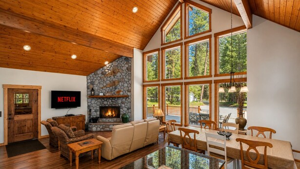 A spacious living room with a stone fireplace, a large dining area, and a television mounted on the wall. - Sauna | Deck | Firepit | Near Lakes | WIFI | BBQ (Leavenworth)
