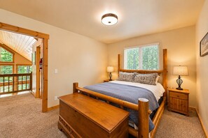 A bedroom with a wooden bed, a nightstand, a dresser, a window with blinds, and a door leading to an outdoor area. - Sauna | Deck | Firepit | Near Lakes | WIFI | BBQ (Leavenworth)