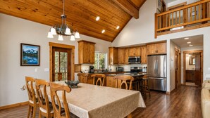 A spacious kitchen with wooden cabinets, a dining area with a table and chairs, and a view of the outdoors through a window. - Sauna | Deck | Firepit | Near Lakes | WIFI | BBQ (Leavenworth)