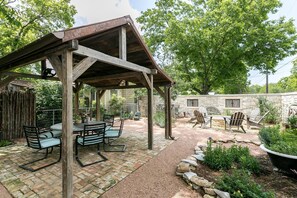 A covered patio with a brick floor, wooden furniture, and a stone wall in the background.