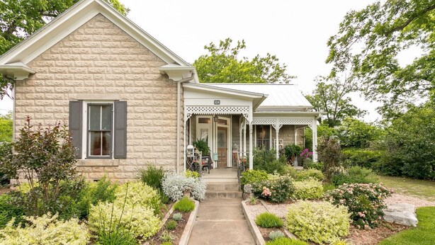 A two-story stone house with a covered porch and a well-maintained garden. - Forget Me Not | Beautiful & Historic | Amazing Outdoor Space (Fredericksburg)