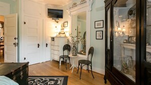 A room with a wooden floor, white doors, a television mounted above a dresser, and a large mirror with a decorative frame. - Forget Me Not | Beautiful & Historic | Amazing Outdoor Space (Fredericksburg)