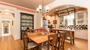 A kitchen with a wooden dining table, chairs, a chandelier, and a decorative arch. - Forget Me Not | Beautiful & Historic | Amazing Outdoor Space (Fredericksburg)