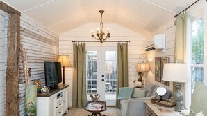 A cozy room with a bed, a sofa, a television, and a chandelier. - Forget Me Not | Beautiful & Historic | Amazing Outdoor Space (Fredericksburg)