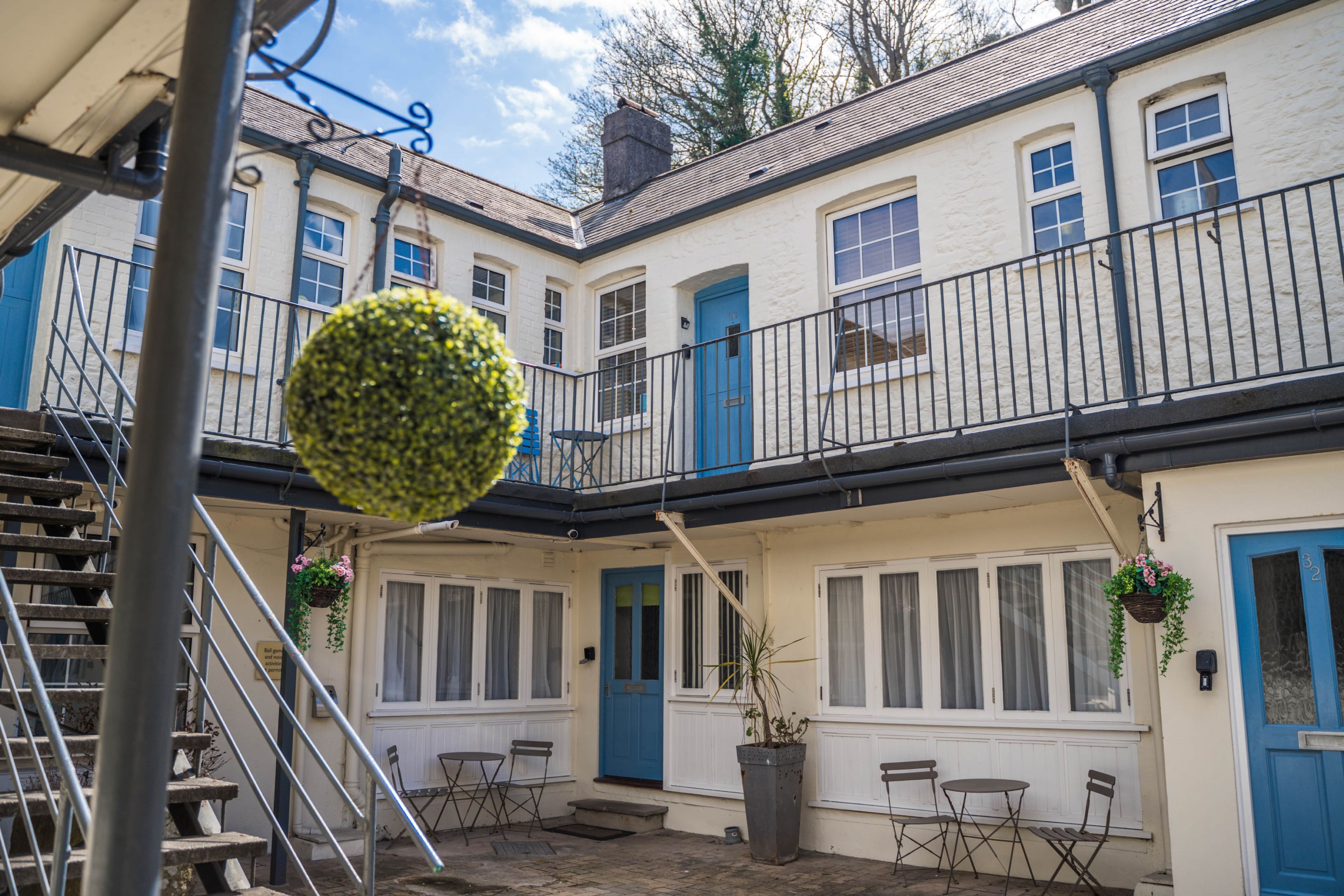 Ein Innenhof mit einer blauen Tür, weißen Wänden und einem Balkon mit schwarzem Geländer.