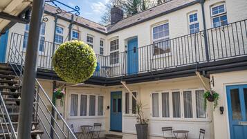 Ein Innenhof mit einer blauen Tür, weißen Wänden und einem Balkon mit schwarzem Geländer.
