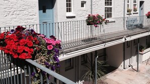 En hvid bygning med flere vinduer og døre, en balkon med gelænder og blomsterkasser.