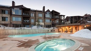Un edificio moderno de varios pisos con área de piscina, que incluye un jacuzzi y una zona de estar techada.