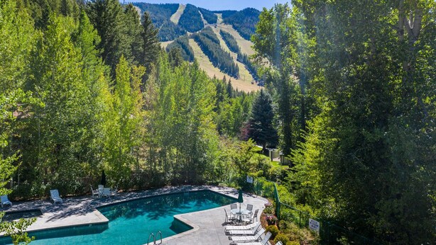 A swimming pool with lounge chairs and a view of a forested hillside. - Seasonal Pool | Pickleball | Hot Tub (Ketchum)