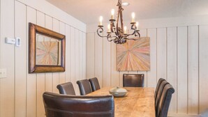 A dining area with a wooden table, six chairs, a chandelier, and two wall-mounted artworks. - Seasonal Pool | Pickleball | Hot Tub (Ketchum)