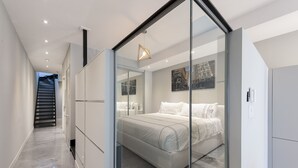 A modern bedroom with a glass partition, a bed with white linens, and a cityscape painting on the wall. - Duplex Loft with Private Terrace, Parc Avenue (Montréal)