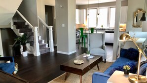 A modern living room with a staircase, a kitchen in the background, and a dining area. - Urban Farmhouse - 3BR 2.5 BA (5 Beds) Near TG Park & Central to Everything! (St. Louis)