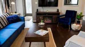 A living room with a blue sofa, a coffee table with magazines, a TV, and a fireplace. - Urban Farmhouse - 3BR 2.5 BA (5 Beds) Near TG Park & Central to Everything! (St. Louis)
