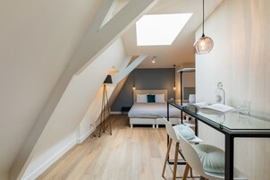 Un dormitorio moderno con tragaluz, cama, mesita de noche y una mesa de comedor de vidrio con sillas.