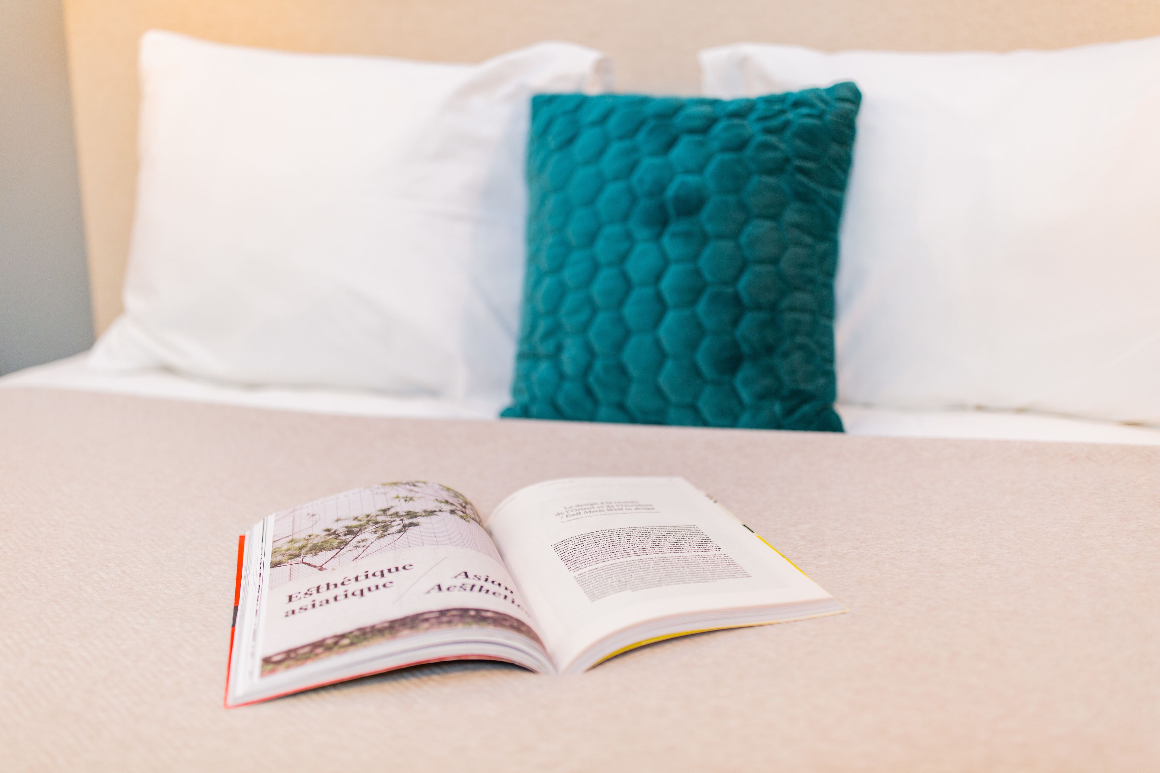 Un libro abierto sobre una cama con almohadas blancas y turquesa.