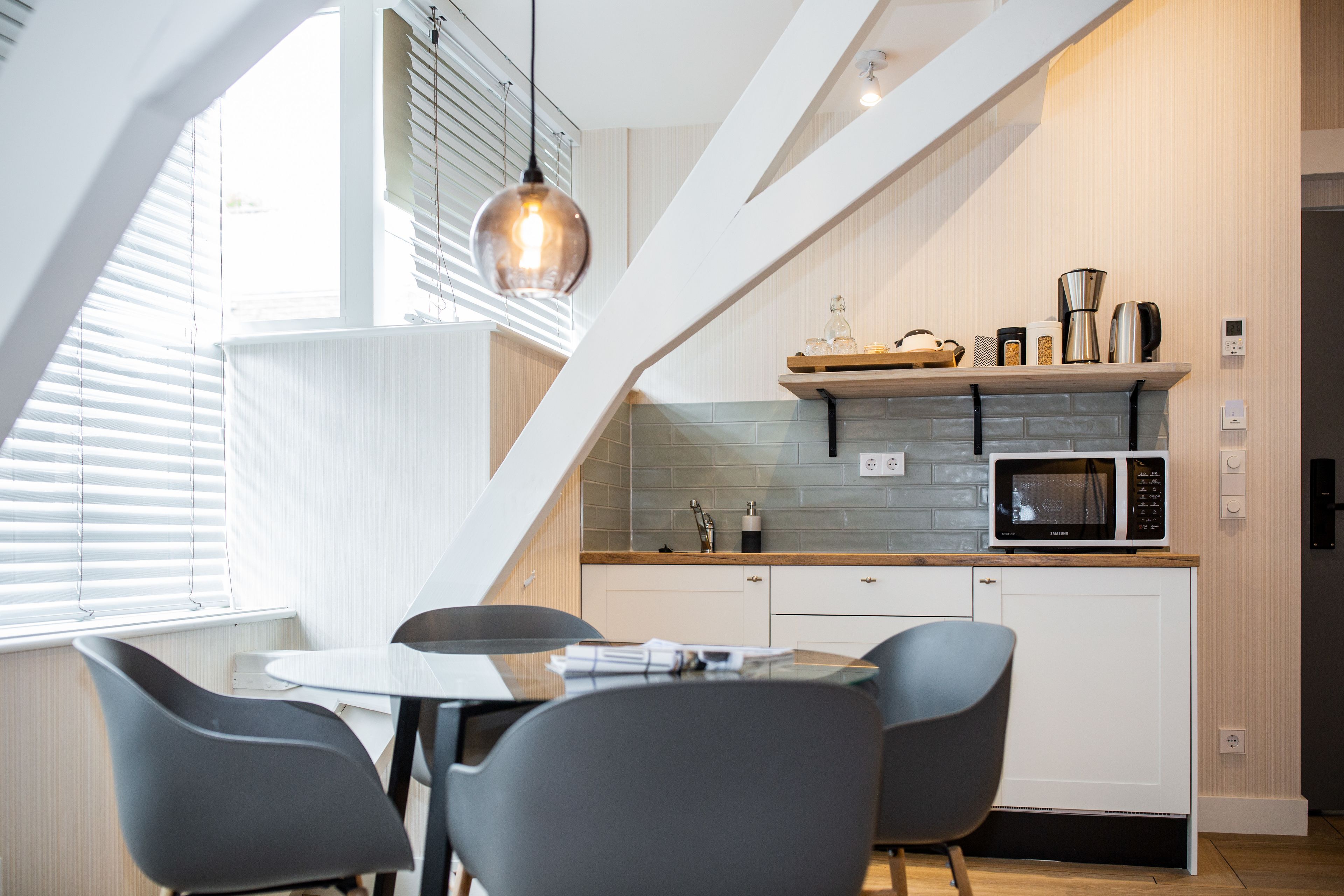 A modern kitchen with a dining area, featuring a microwave, coffee maker, and a hanging light fixture.
