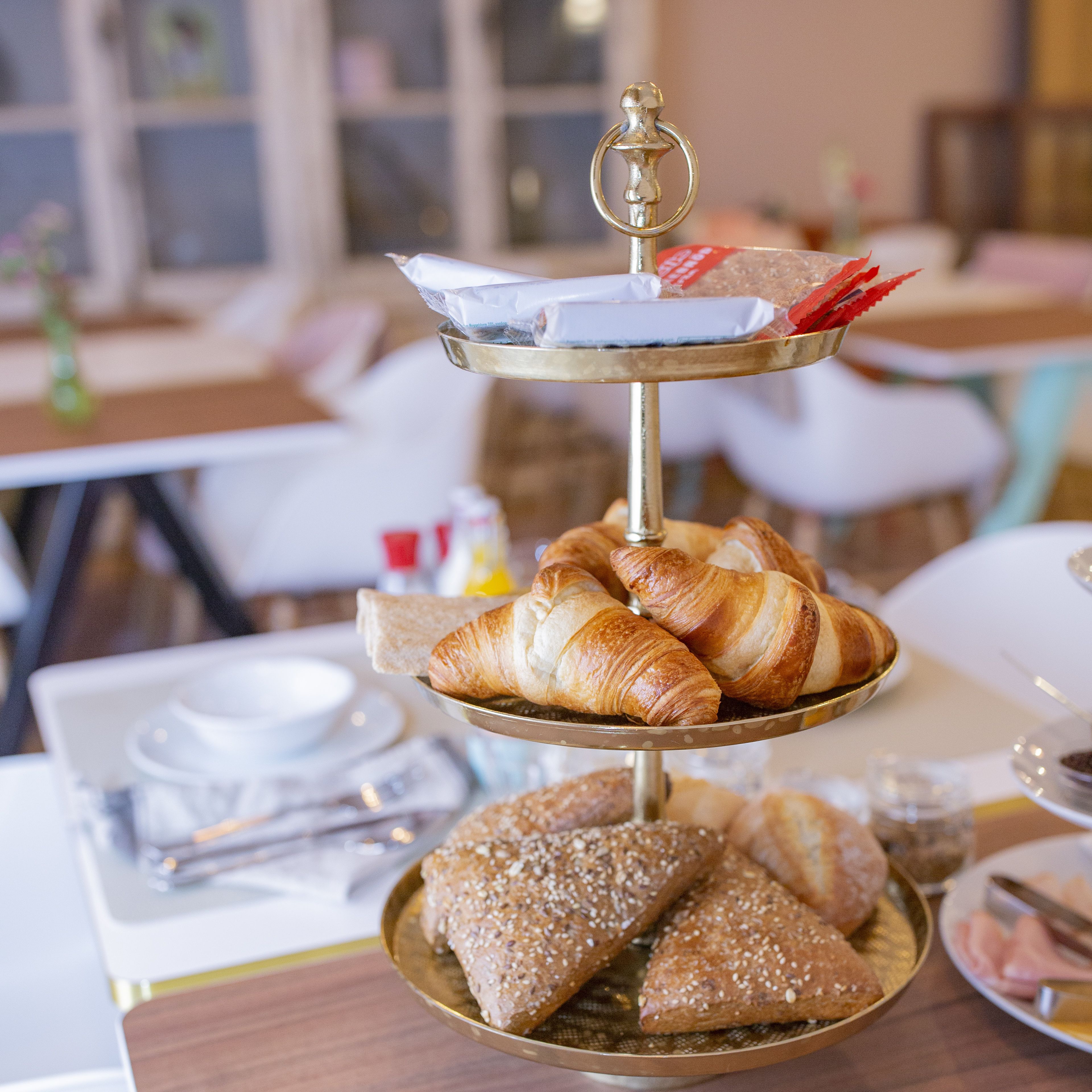 A three-tiered serving tray with pastries and bread, set on a table in a dining area.