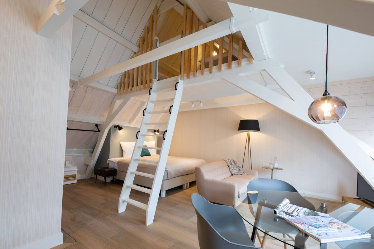 A loft-style bedroom with a wooden staircase, a bed, a desk, and a chair.