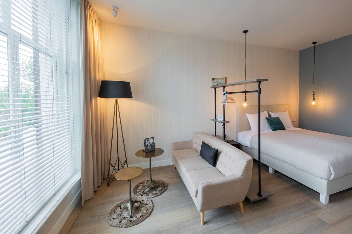 A modern hotel room with a bed, a sofa, a small table, and a lamp.