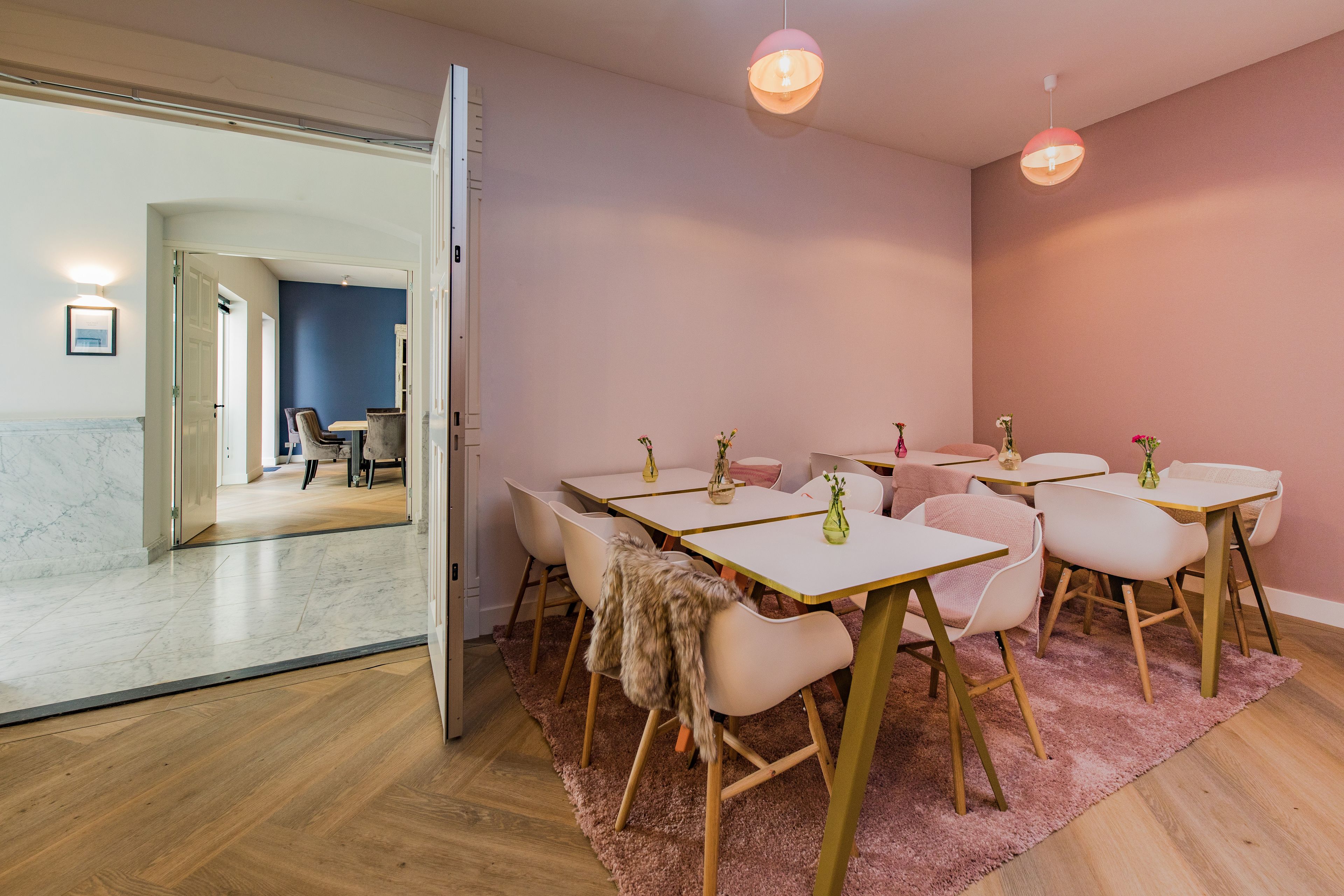 A modern room with a wooden floor, white and pink chairs, and a pink rug.