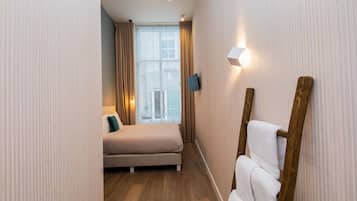 A hotel room with a bed, a TV mounted on the wall, and a wooden ladder leaning against the wall.