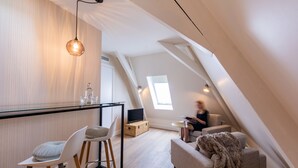 A modern loft bedroom with a sloped ceiling, a glass dining table, a sofa, and a large window providing natural light. - Stadsvilla Mout (Schiedam)