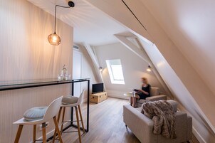 Un dormitorio tipo loft moderno con techo inclinado, una mesa de comedor de vidrio, un sofá y un amplio ventanal que proporciona luz natural.