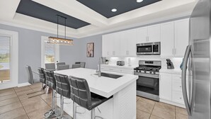 A modern kitchen with white cabinetry, a central island with bar stools, stainless steel appliances, and a pendant light.