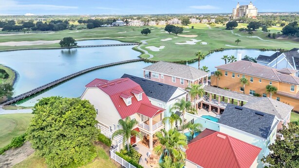 A multi-story hotel with a red roof, a pool, and a view of a golf course and lake.