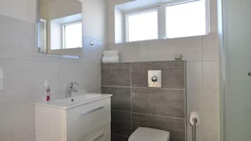 A modern bathroom with a white vanity, a toilet, and a shower area.
