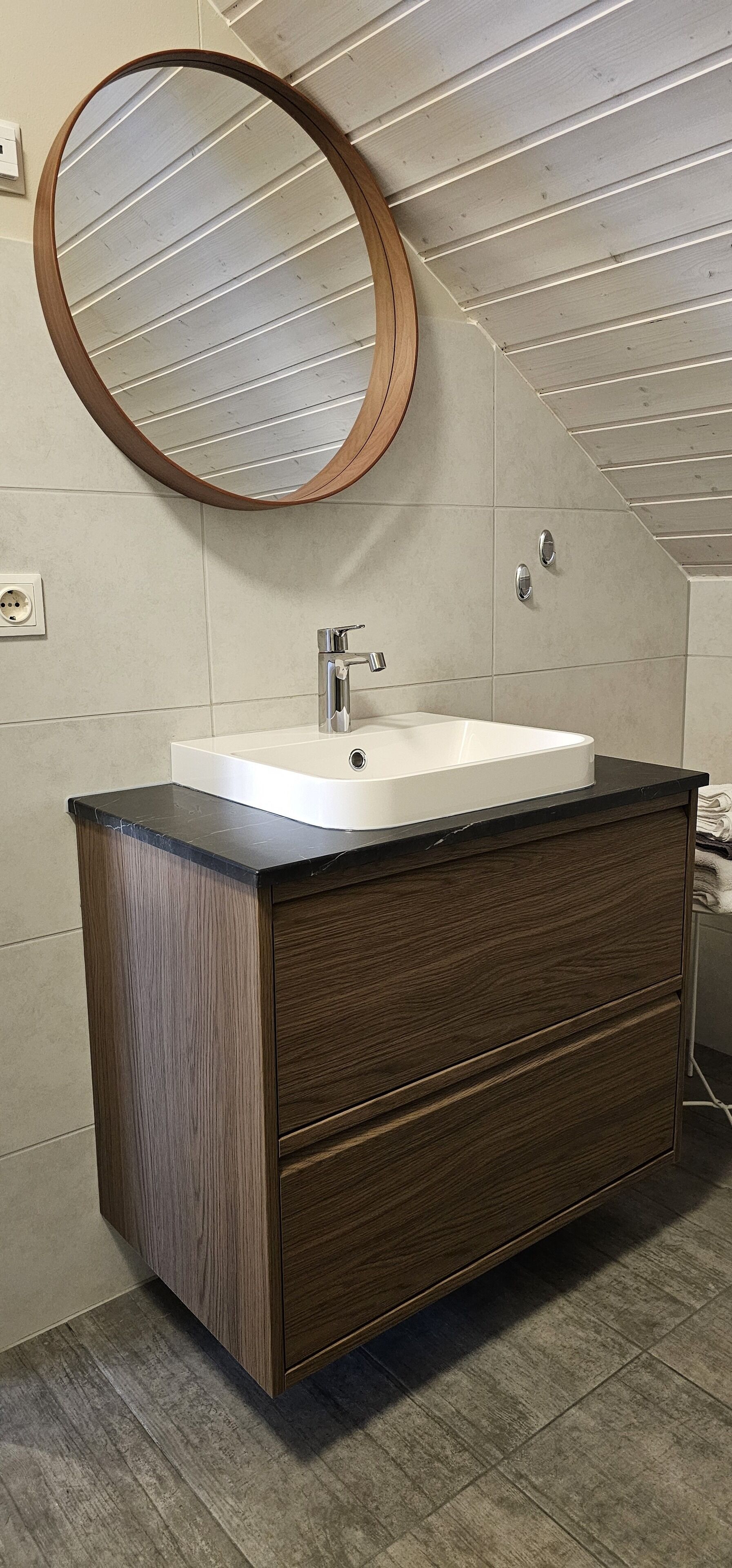 Un bagno con un mobile contenitore in legno, un lavandino bianco e uno specchio rotondo.