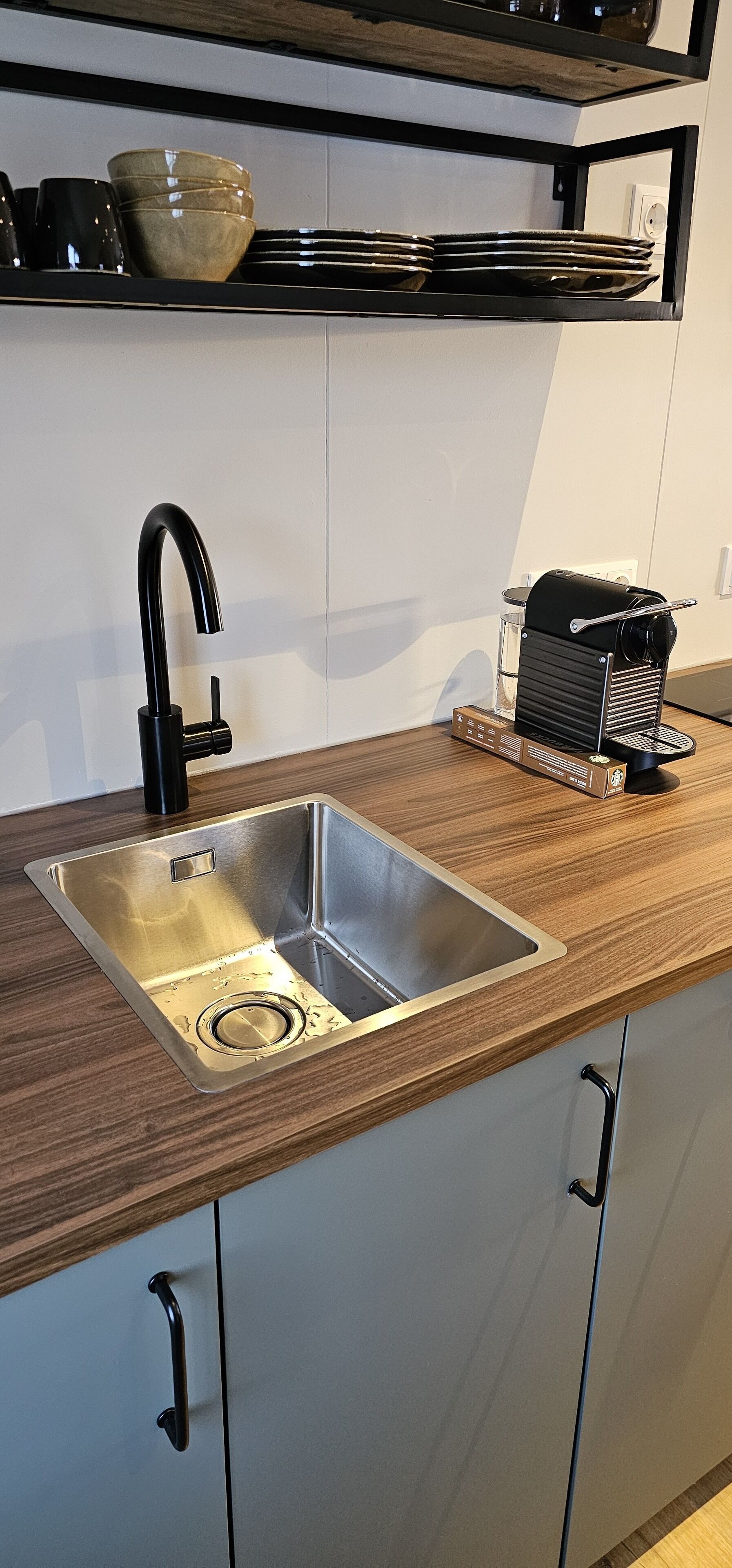 Cozinha moderna com pia de aço inoxidável, torneira preta e máquina de café no balcão.