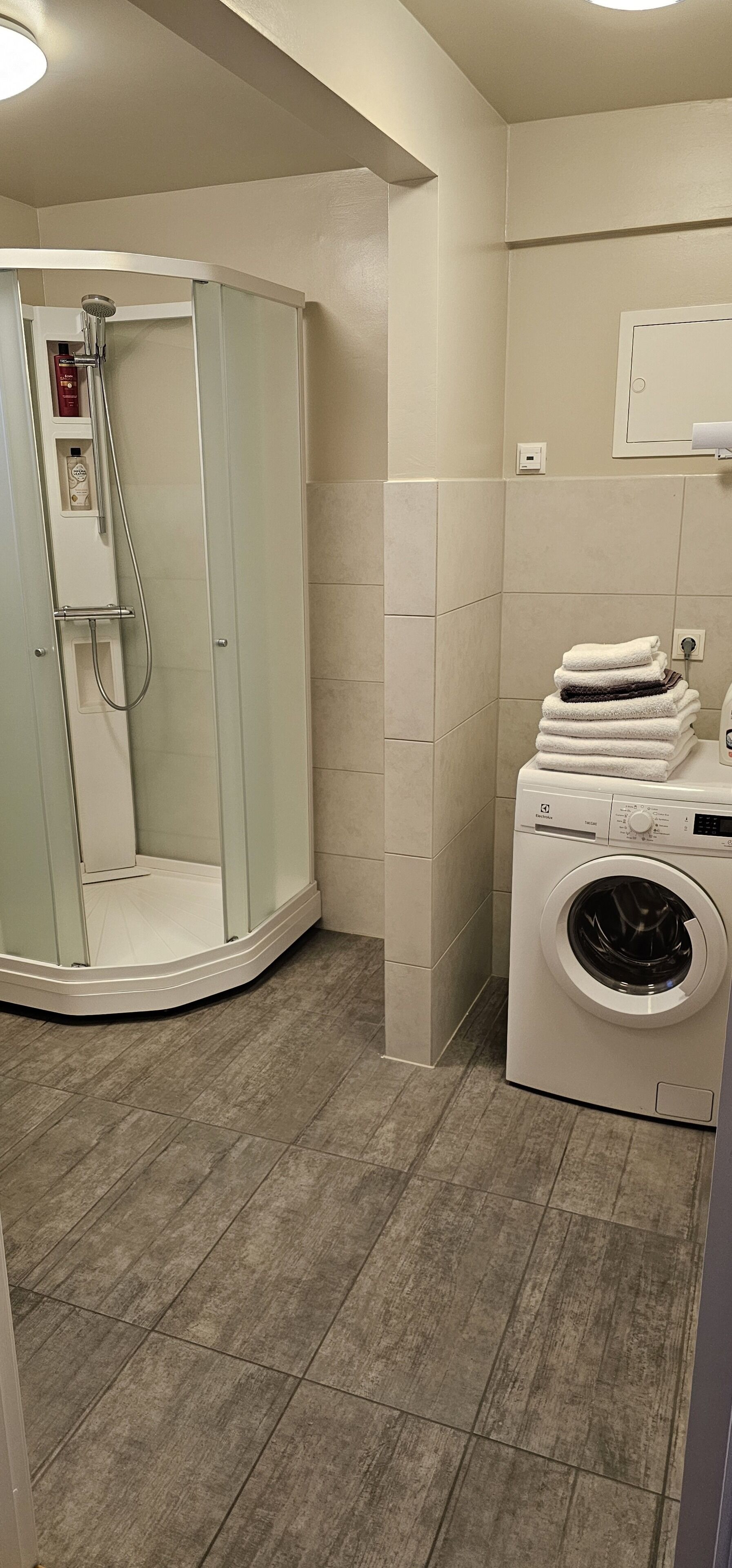Un baño moderno con ducha de vidrio, lavadora integrada y toallas ordenadas.