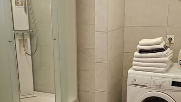 Un baño moderno con ducha de vidrio, lavadora integrada y toallas ordenadas.