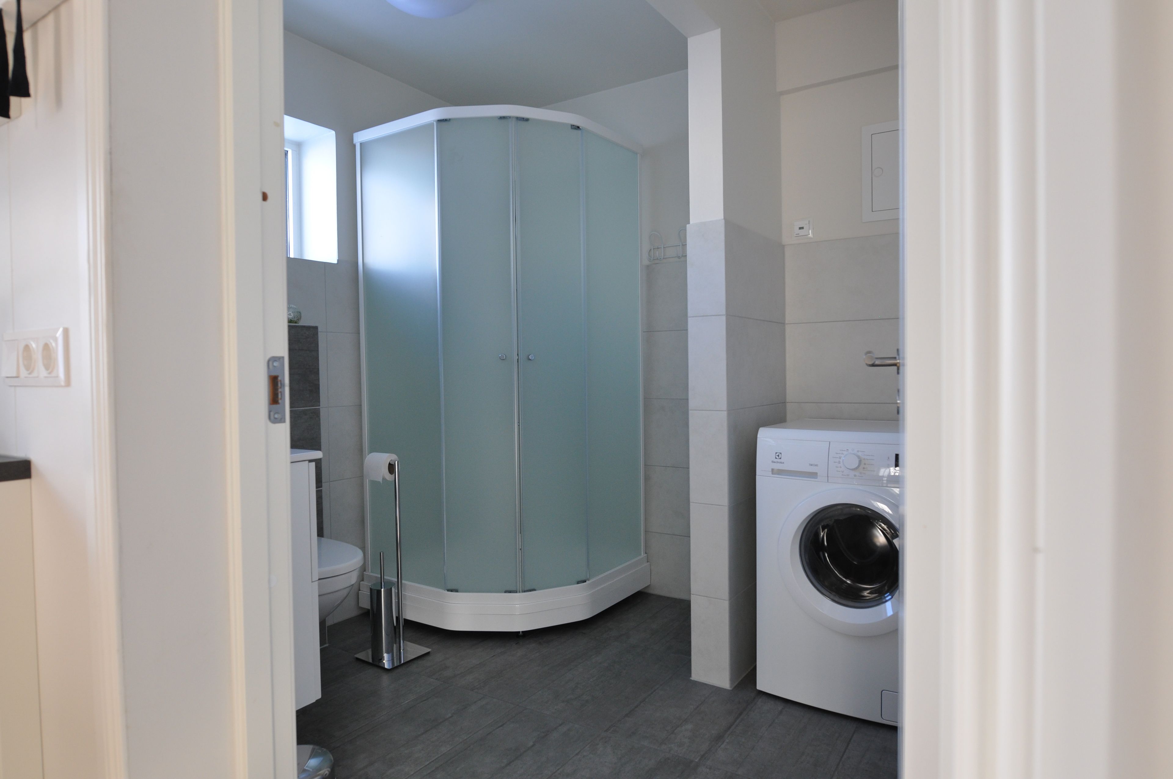 A modern bathroom with a corner shower, a toilet, and a washing machine.