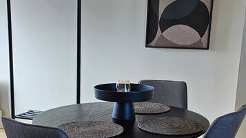 Un comedor con una mesa redonda, cuatro sillas, una lámpara colgante negra y una obra de arte en la pared.