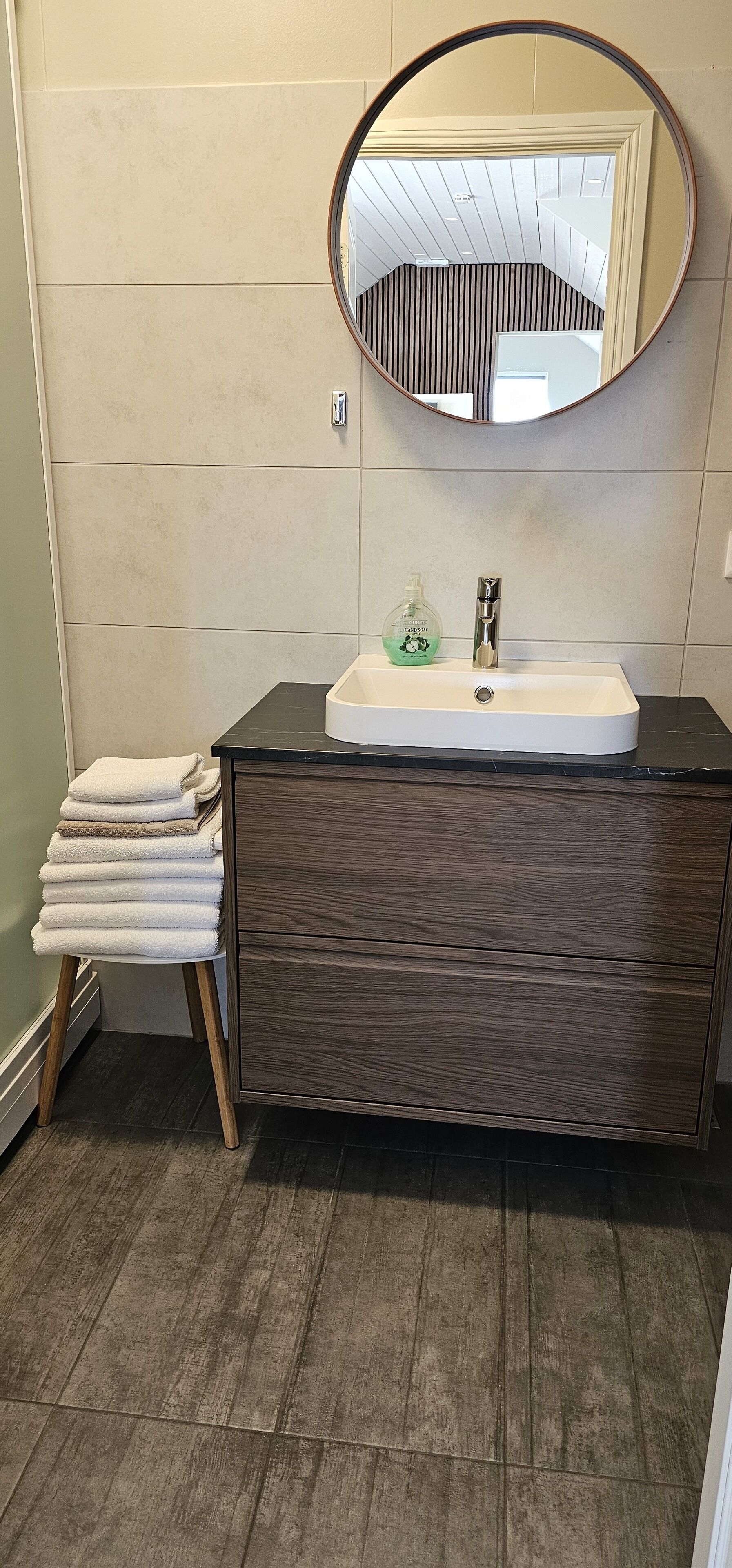 A bathroom with a white sink, dark wood vanity, a mirror, and a towel rack.
