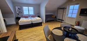 A cozy loft bedroom with a loft bed, a sofa, a dining table with chairs, and a TV mounted on the wall. - Kviholmi Premium Apartments (Rangárþing eystra)