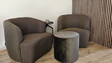 Deux fauteuils recouverts d’un tissu texturé, un petit pouf rond et une table d’appoint noire agrémentée d’un objet décoratif.