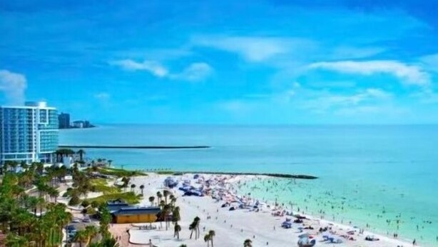 A beach resort with a large building on the left, a sandy beach, and clear blue water. - Brand new private pool with lake view minutes to the parks! (Kissimmee)
