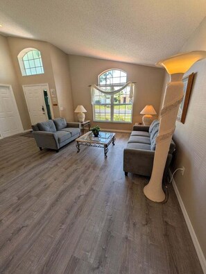 A spacious living room with hardwood flooring, two sofas, a coffee table, and a large window with a view. - Brand new private pool with lake view minutes to the parks! (Kissimmee)
